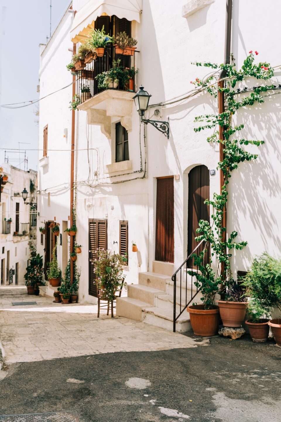 Sunny Italian street with potted plants and white buildings.